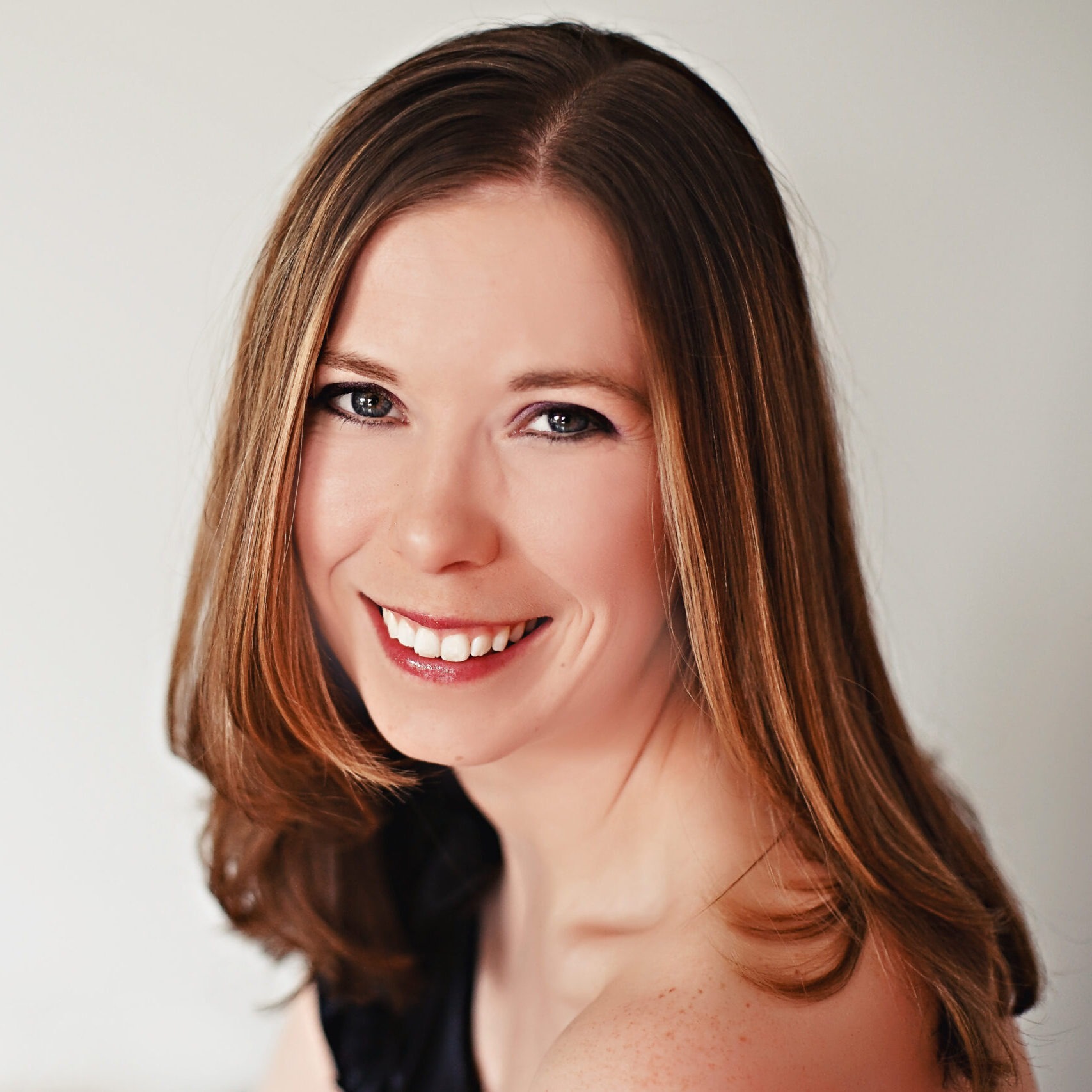 A Smiling Woman with Long Brown Hair Posing Against a Plain Light Background